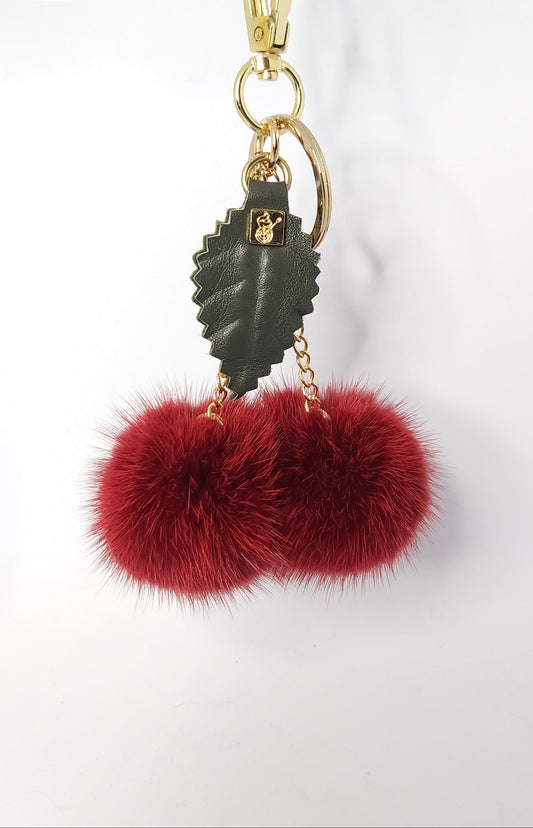 Keychain with red fur pom-poms and gold accents on a white background