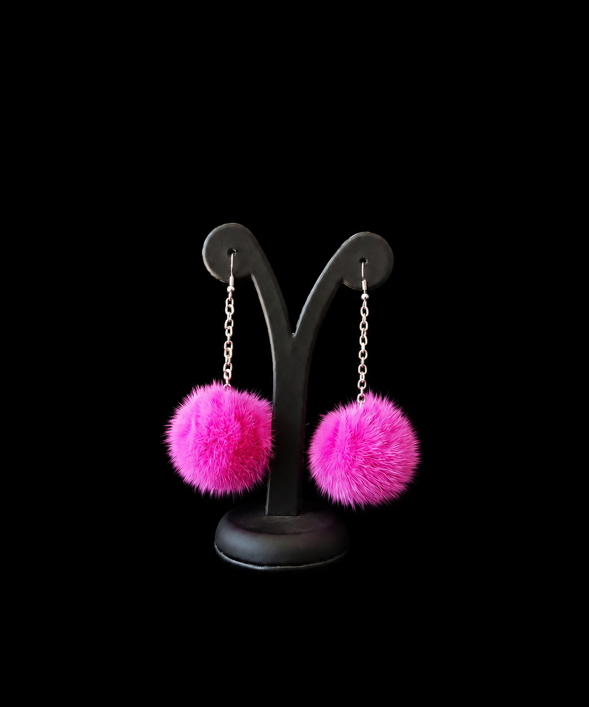 Pink fuzzy earrings on a black stand against a black background