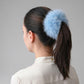 Female with a blue fluffy hair accessory in their ponytail against a gray background