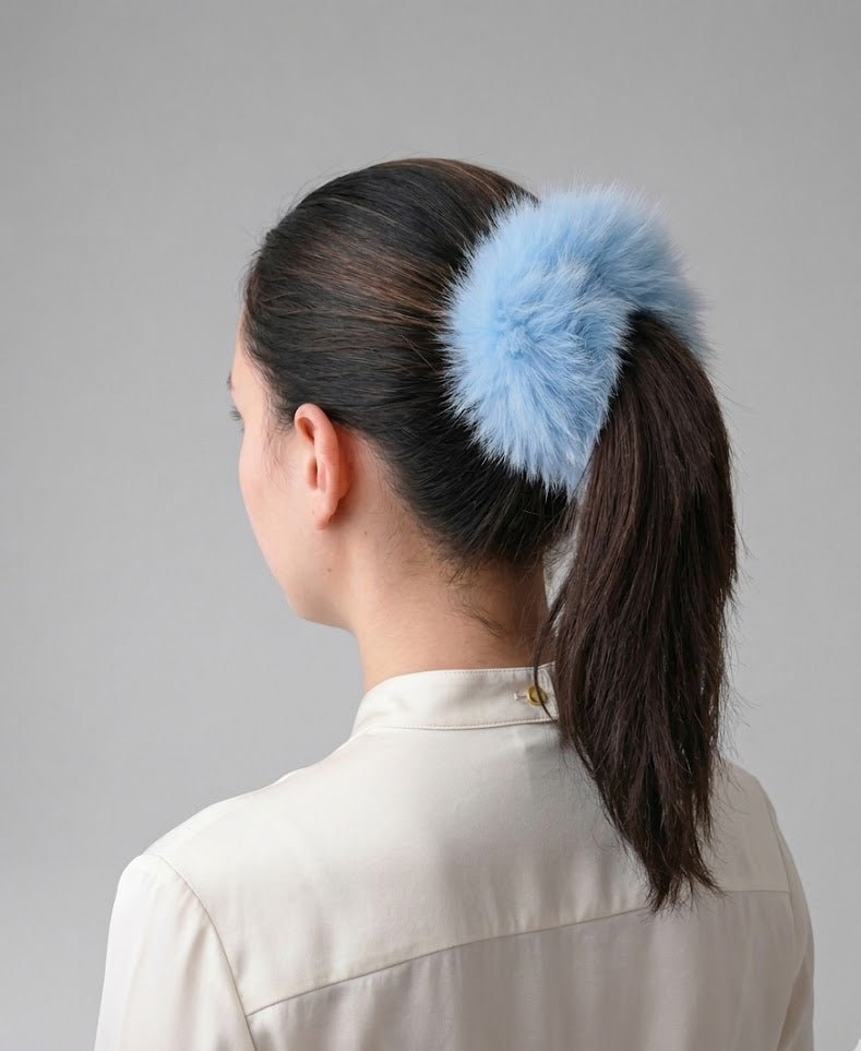 Female with a blue fluffy hair accessory in their ponytail against a gray background